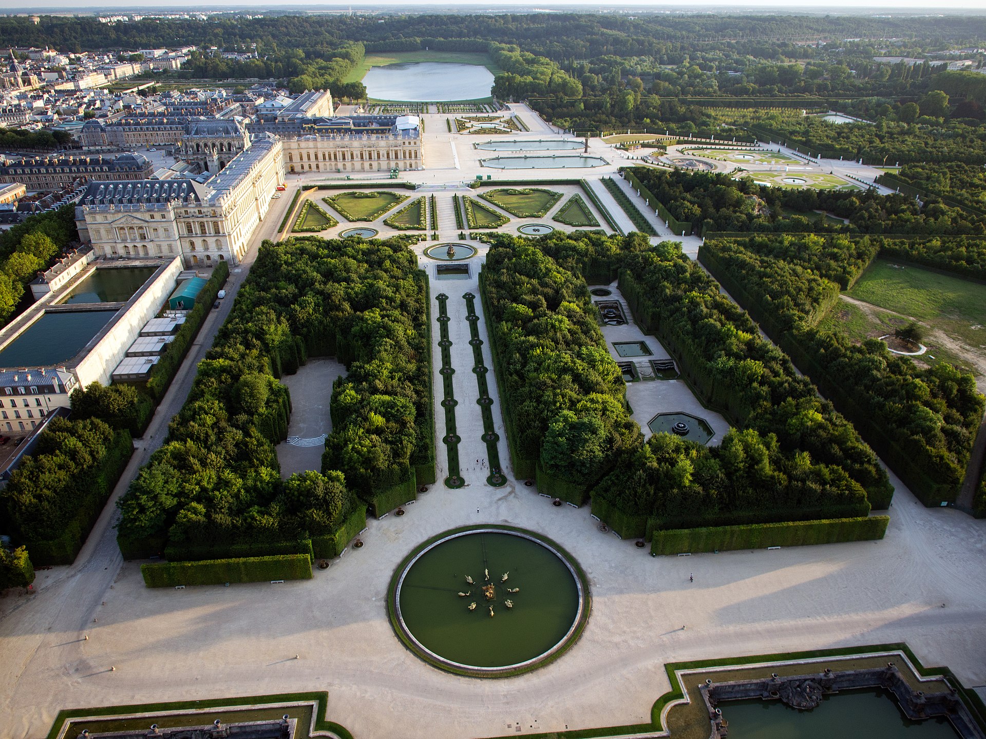 Au premier plan, le bassin du Dragon marque le point de départ de l'Allée d’Eau, rythmée de part et d’autre par quatorze fontaines, menant au Bassin des Nymphes puis au Bassin de la Pyramide.